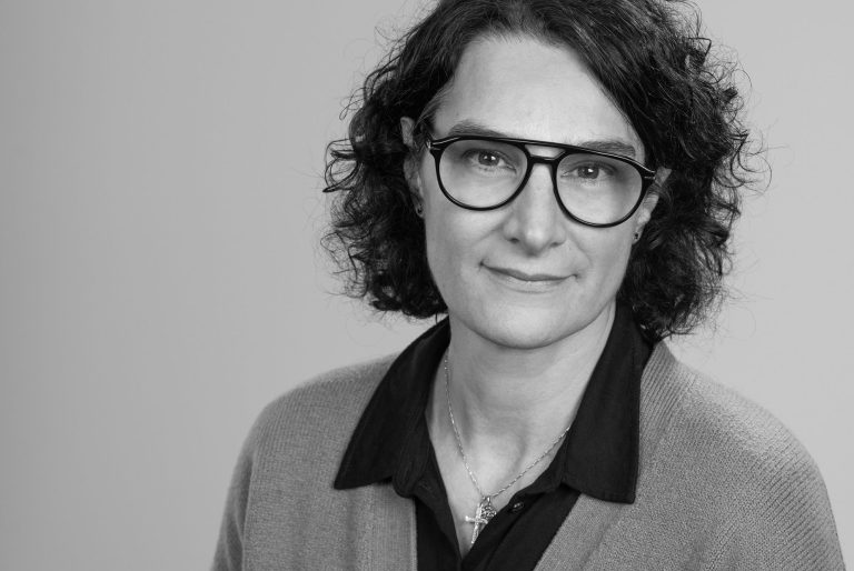 Master in Business Sciences (Uni. Mannheim) Person mit lockigem Haar, Brille und einem grauen Oberteil, neutraler Gesichtsausdruck.